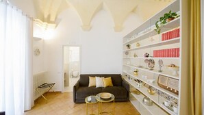 Un salon comprenant un canapé, deux petites tables rondes et une bibliothèque remplie d’objets décoratifs.