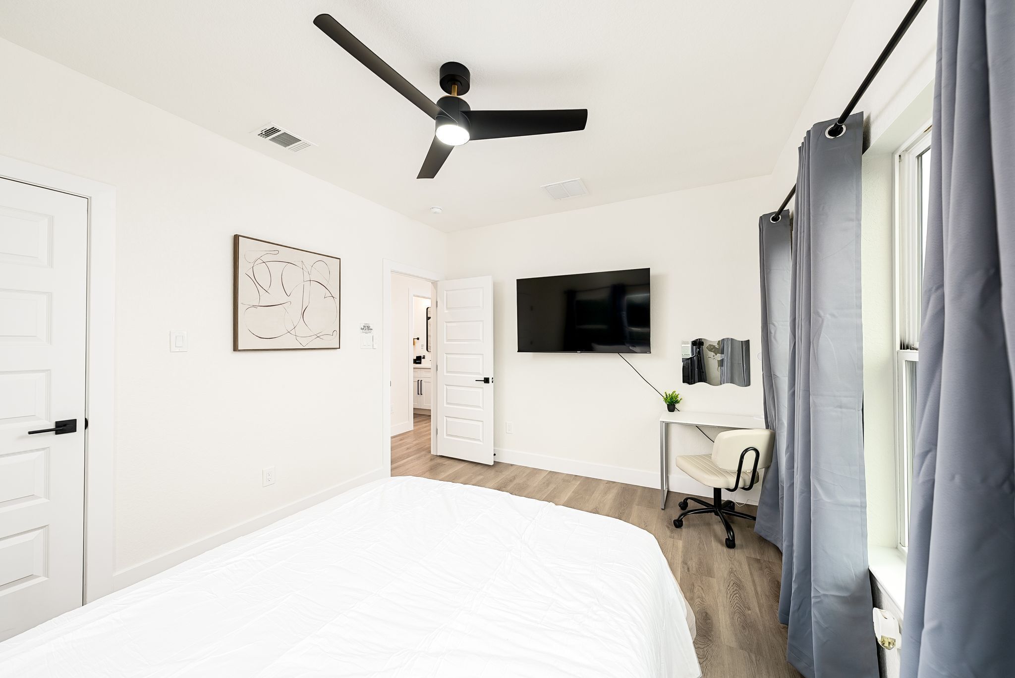 Une chambre moderne avec un lit, un ventilateur de plafond, une télévision et un bureau avec une chaise.