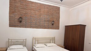 A room with two single beds, a wooden wardrobe, and a brick wall with two wall-mounted lights.