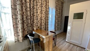 A compact kitchen with a dining area, featuring a wooden table, two bar stools, and a window with curtains.
