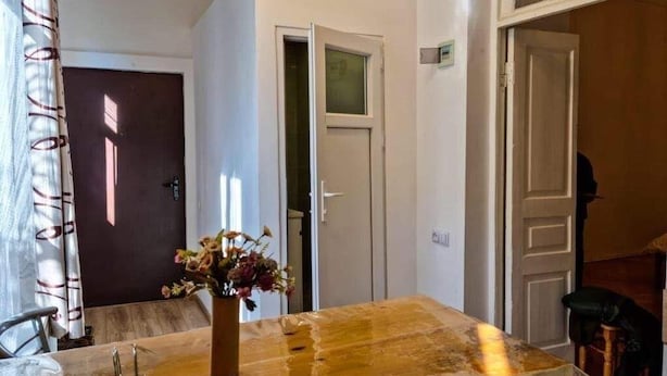 A room with a wooden table, a vase with dried flowers, and a door leading to another room.