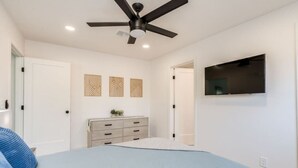 Une chambre à coucher comprenant un lit, une commode, un ventilateur de plafond et un téléviseur fixé au mur.