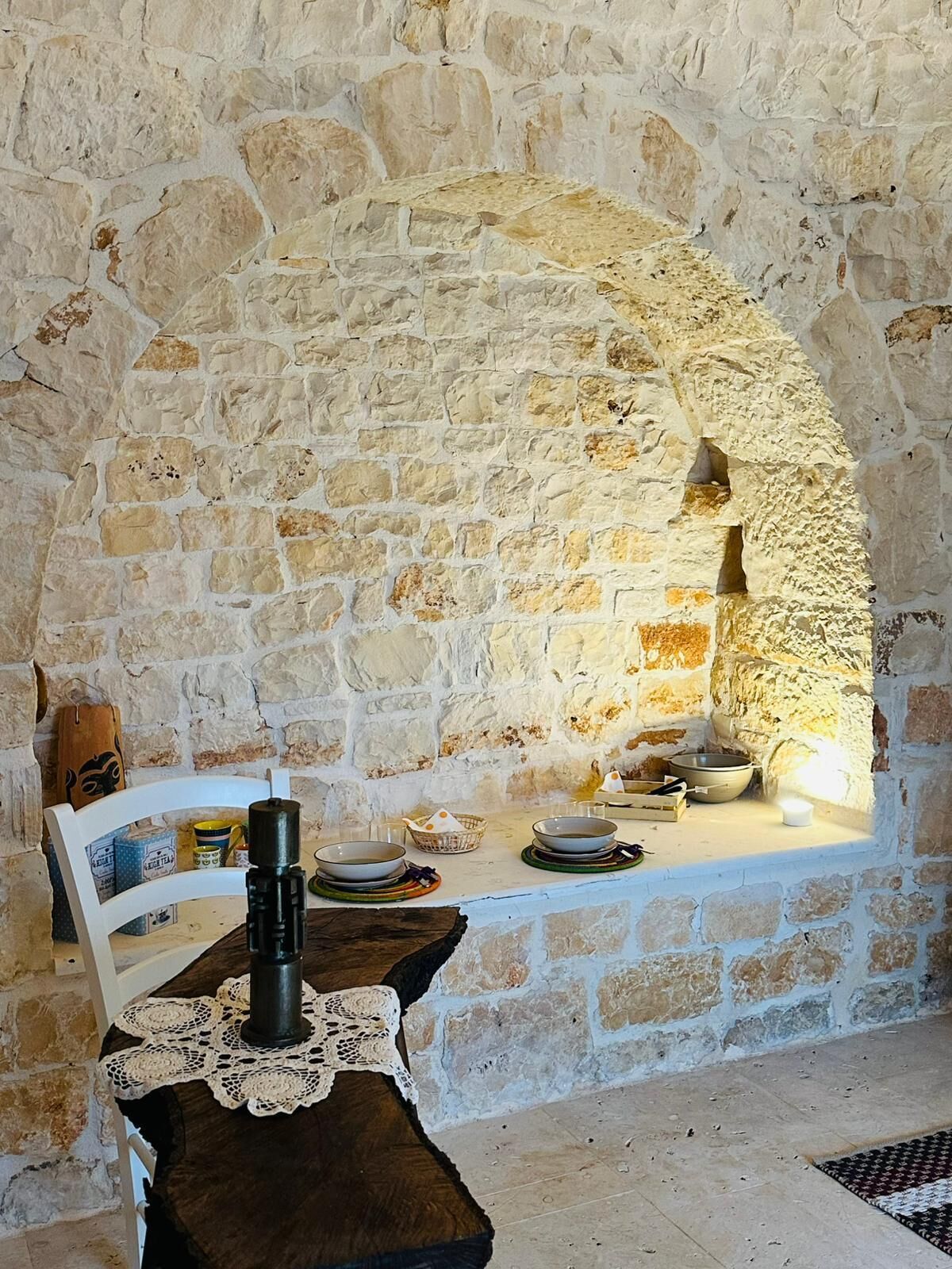 A stone-walled room with a table set for dining, a candle, and a rustic wooden table.