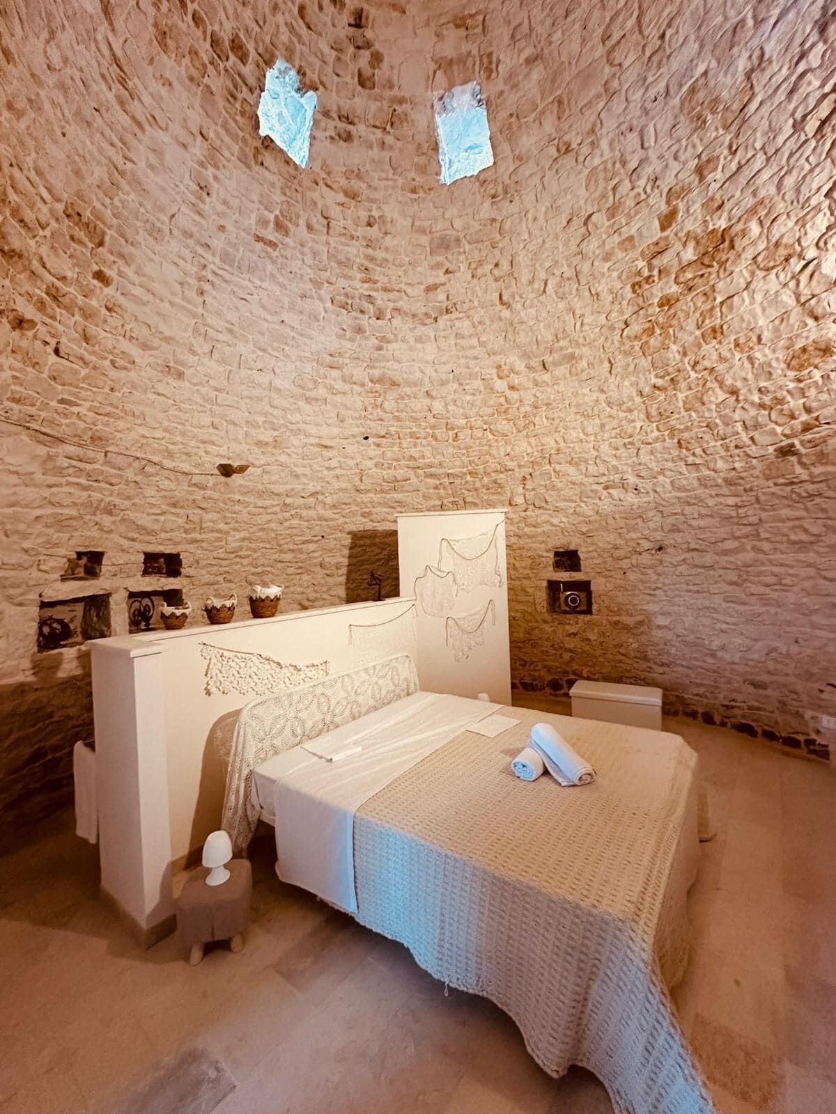 A cozy, stone-walled bedroom with a bed, bedside tables, and a small stool.
