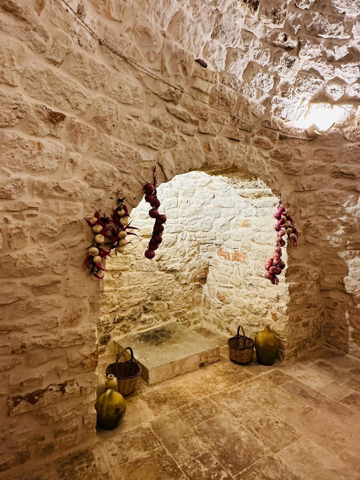 A stone-walled alcove with a small step leading up to a niche. Decorative gourds and a basket are placed on the floor.