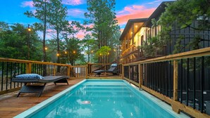 A pool area with lounge chairs and a wooden deck, surrounded by trees and a building with large windows. - 2Mountaintop Cabins Pool Saunas Slides Views &More (Broken Bow)