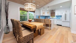 A spacious kitchen with wooden flooring, white cabinets, and a dining area with a wooden table and woven chairs. - 2 Private Living Spaces, 2 Hot Tubs and Bikes! (Kill Devil Hills)