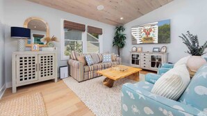 A spacious living room with a wooden ceiling, a striped sofa, a blue sofa with fish patterns, a wooden coffee table, and a large mirror. - 2 Private Living Spaces, 2 Hot Tubs and Bikes! (Kill Devil Hills)