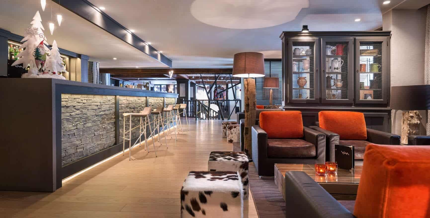 A modern lobby with a stone wall, seating area with leather sofas, a bar with a stone countertop, and a large cabinet with glass doors.