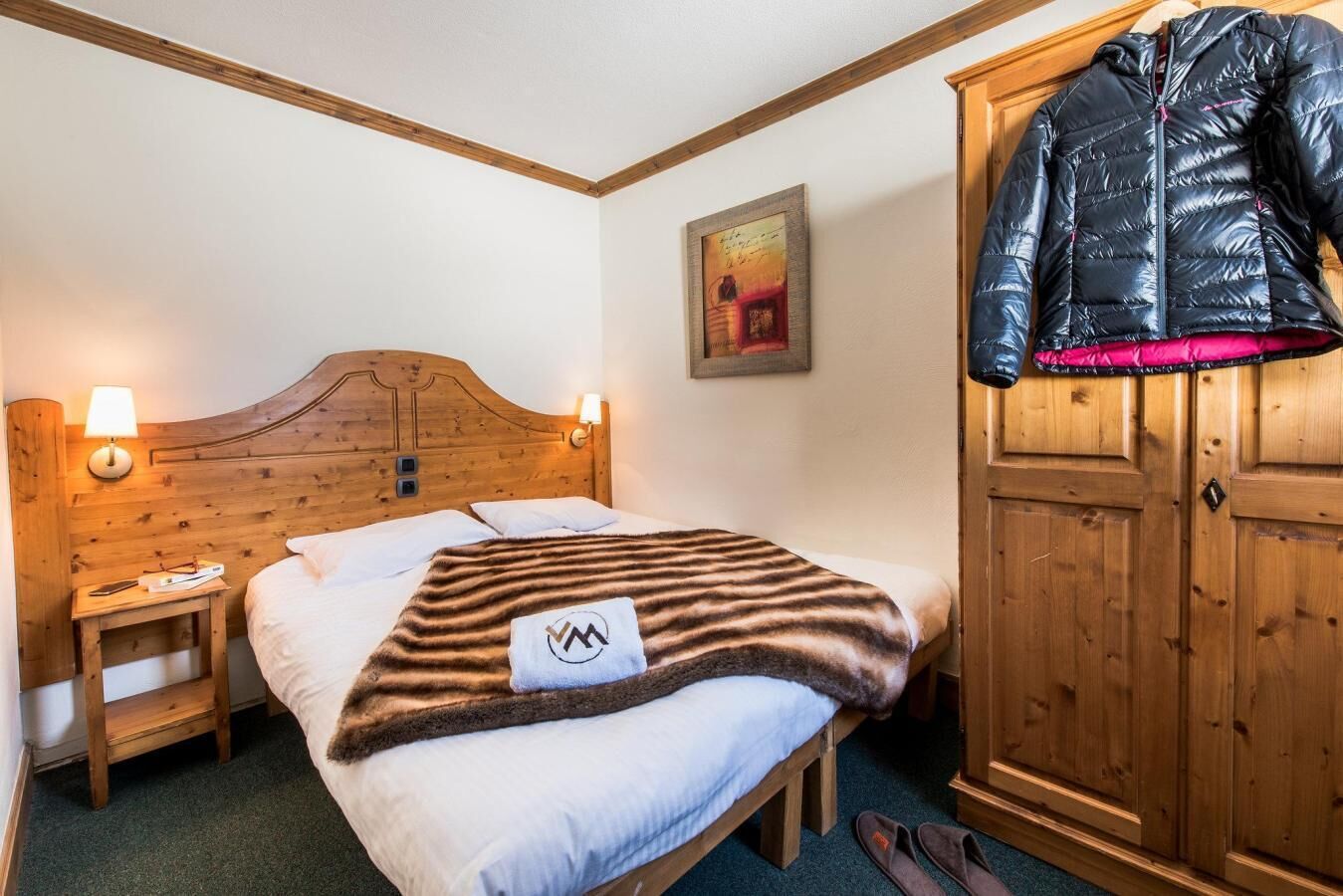 A hotel room with a wooden headboard, a bed with a striped blanket, a nightstand with a lamp, and a wardrobe.