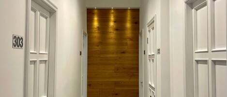 A hallway with white doors, a wooden wall at the end, and a number "303" on the left wall.