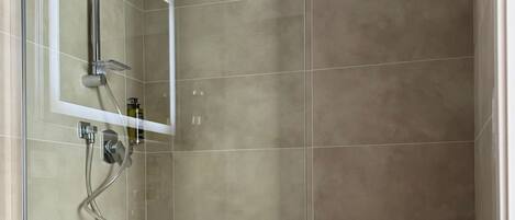 A modern bathroom with a shower, a mirror, and a wooden shelf.