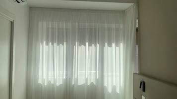 A hotel room with a bed, a bedside table, a wall-mounted phone, and sheer curtains.