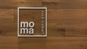 Un cartel enmarco con el texto 'mo ma URBAN STAY' sobre un suelo de madera.