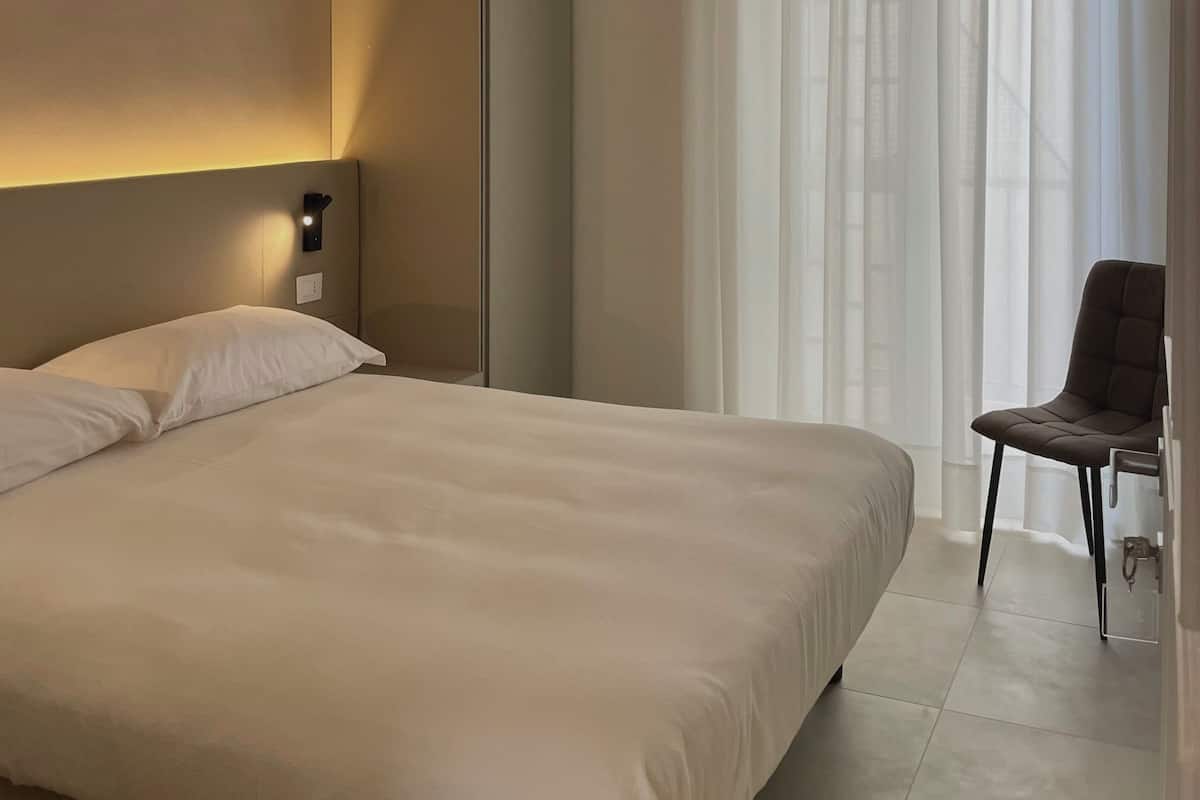 A modern hotel room with a large bed, a chair, and a wardrobe.
