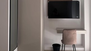 Una habitación moderna y minimalista con una televisión de pantalla plana montada en la pared, un escritorio pequeño con una silla y un cubo de basura.