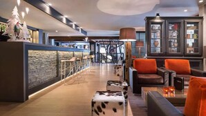 Un hall d’entrée moderne avec un mur en pierre, un espace salon doté de canapés en cuir, un bar avec un comptoir en pierre et un grand meuble avec des portes en verre.