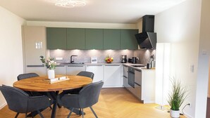 Una cocina moderna con armarios verdes, una mesa de comedor de madera con sillas y una planta en maceta.