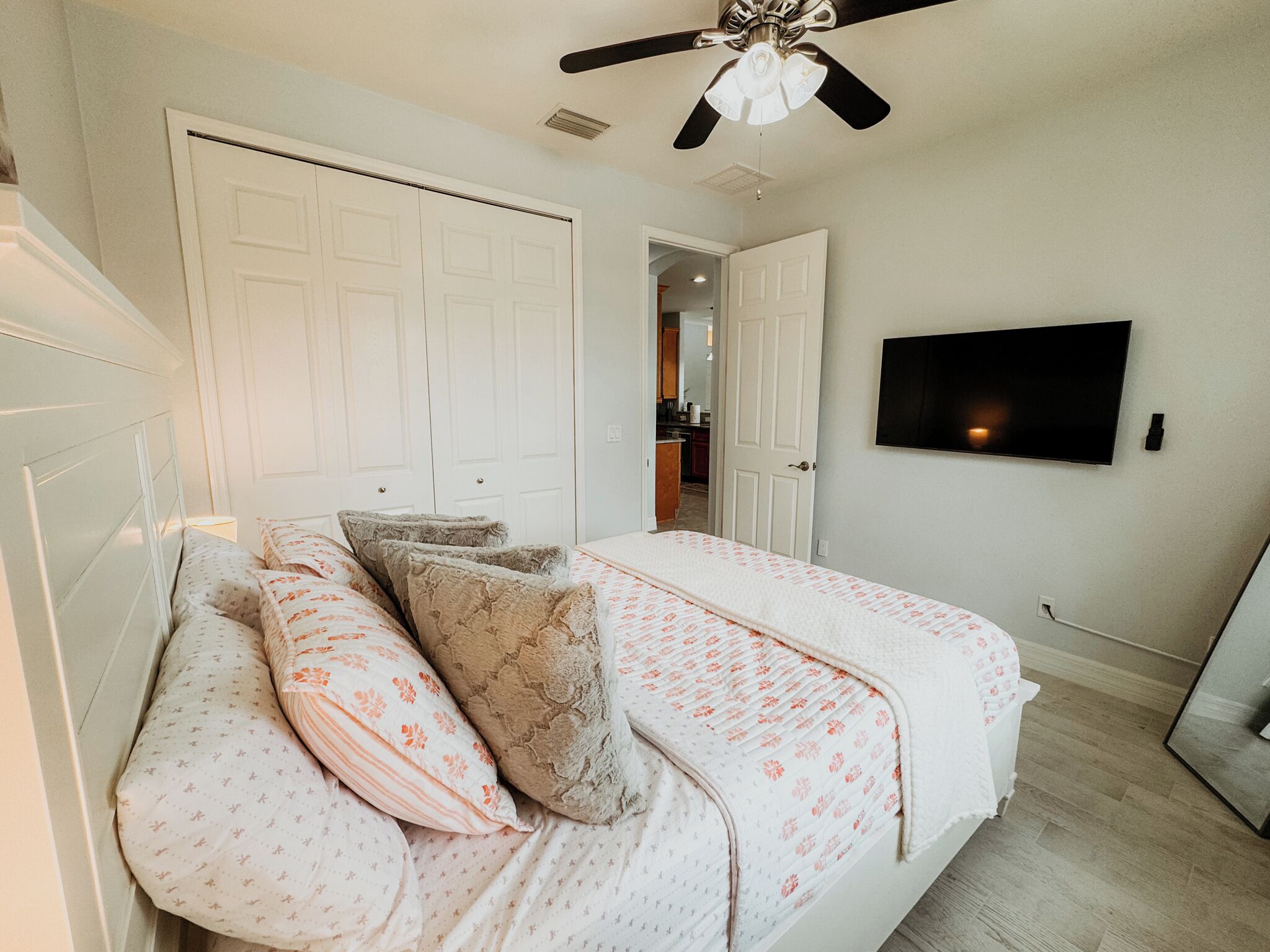Un dormitorio con cama, ventilador de techo, televisión y puerta que da a una cocina.