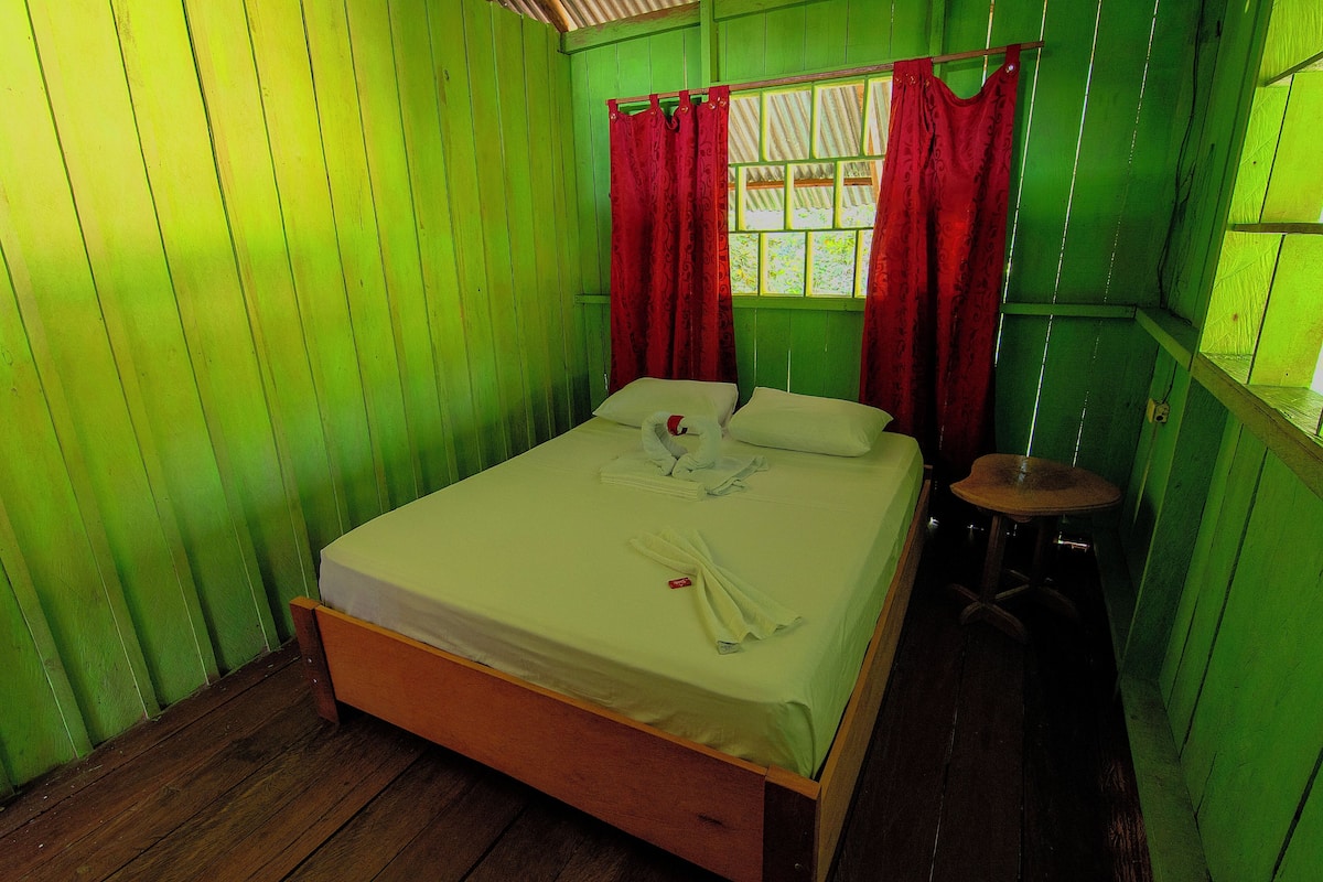 A room with green walls, a wooden bed, a small stool, and a window with red curtains.