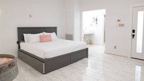 A bedroom with a bed, white walls, a door, and a radiator.