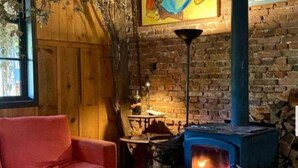 A cozy room with a red sofa, a table with magazines, a brick wall, a blue wood-burning stove, and a window with a view of trees. - Parador Hampel (Sao Francisco de Paula)