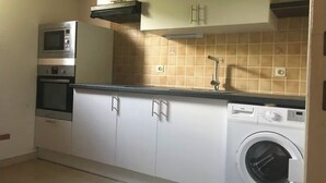 A compact kitchen with white cabinets, a built-in microwave, an oven, a sink, and a washing machine.