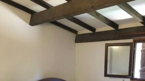 A bedroom with a bed, a window, and wooden beams on the ceiling.