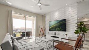 A modern living room with a sofa, coffee table, TV, and a balcony with a view. - 3 BD/ 2 BA / Storey Lake (3131-306 PC) (Kissimmee)