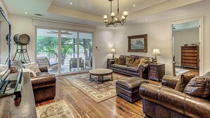 A spacious living room with leather sofas, a coffee table, and a chandelier. - Lakefront 6BR | Ramp, Dock, Views | Sleeps 12 (Kingsland)