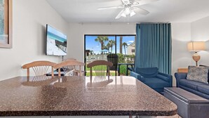 A modern kitchen with granite countertops, wooden chairs, a ceiling fan, and a large window with a view of the outdoors. - Blue Surf 16A (Miramar Beach)