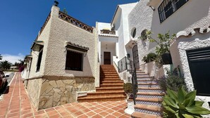 A traditional building with a stone facade, a tiled entrance, and a staircase leading to a door. - R1384 | Casa Cleo nº 22 (Nerja)