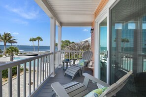 A balcony with two lounge chairs, a small table, and a view of the ocean.