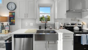 A modern kitchen with white cabinetry, stainless steel appliances, a window with a view, and a clock on the wall. - Adventure Included, Water views, Bikes & Kayak (Jensen Beach)