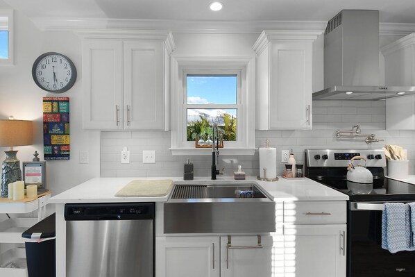 A modern kitchen with white cabinetry, stainless steel appliances, a window with a view, and a clock on the wall.