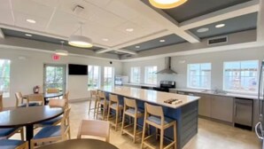 A modern kitchen with a central island, bar stools, and a dining area with round tables. - Adventure Included, Water views, Bikes & Kayak (Jensen Beach)