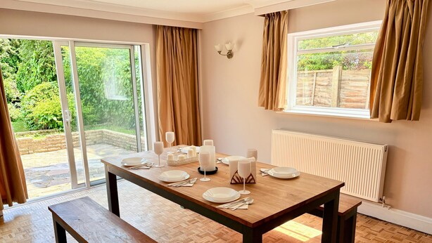 A dining area with a wooden table set for four, a bench, and a view of greenery outside. - 6 Bed House on Prime Private Road in Ickenham (Ickenham)