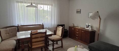 A living room with a dining table, chairs, a sofa, a cabinet, and a lamp.