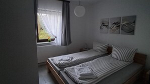 A bedroom with a bed, a window with curtains, a wall-mounted light, and a small table. - Beautiful vacation apartment in Himmelberg for a vacation. (Thalfang)