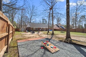 A backyard with a wooden deck, a swing set, and a play area with a bench and cushions.