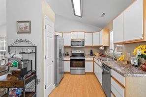 A compact kitchen with white cabinets, stainless steel appliances, and a coffee bar area.