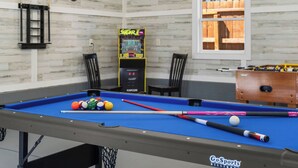 A pool table with balls and cues, a foosball table, and a neon arcade game in a room with a wooden wall and a window. - Charming 3-bedroom Home in Monroe with a Pool Table and Fire Pit, WiFi (Monroe)