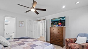 A bedroom with a bed, a dresser, a chair, a ceiling fan, and a TV mounted on the wall. - Charming 3-bedroom Home in Monroe with a Pool Table and Fire Pit, WiFi (Monroe)