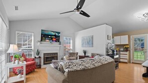 A spacious living room with a fireplace, a television mounted on the wall, and a ceiling fan. - Charming 3-bedroom Home in Monroe with a Pool Table and Fire Pit, WiFi (Monroe)