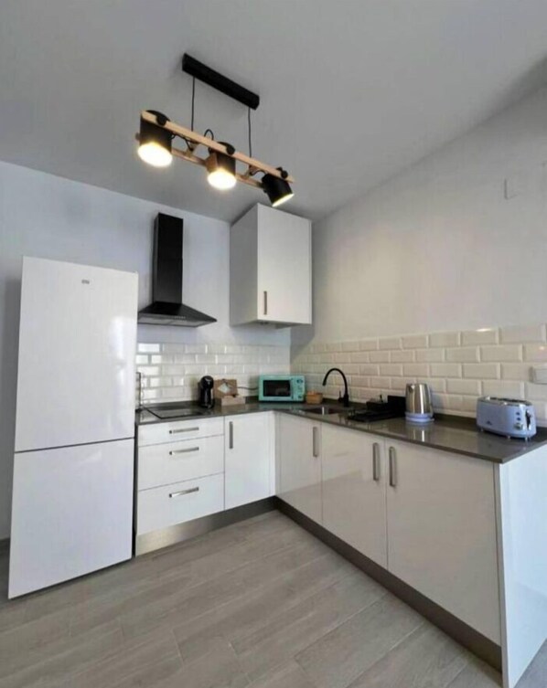 A modern kitchen with white cabinets, a black range hood, a microwave, a kettle, and a toaster.