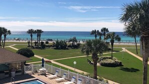 A pool area with lounge chairs, a small building, and a view of the ocean. - Blue Surf 16B (Miramar Beach)