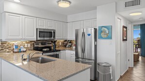 A modern kitchen with white cabinets, stainless steel appliances, a granite countertop, and a view to the outdoors. - Blue Surf 16B (Miramar Beach)