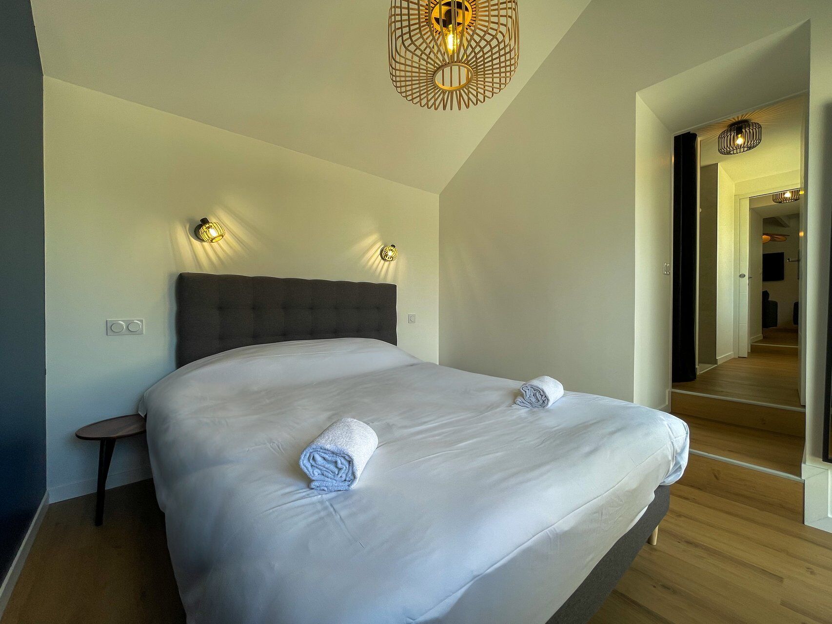 Une chambre d’hôtel moderne avec un grand lit, deux lampes fixées au mur, une petite table et un miroir.