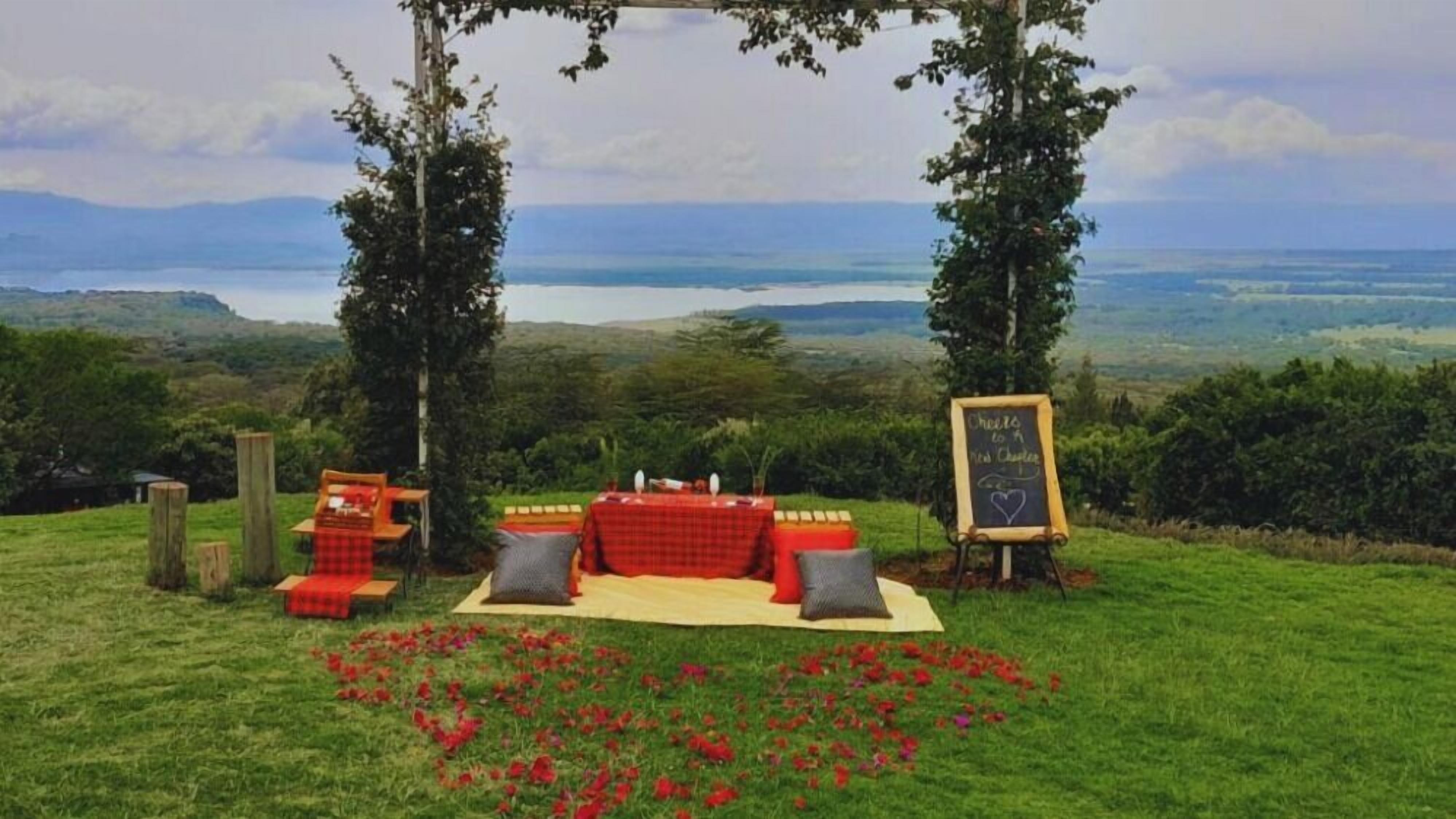 An outdoor seating area with a table and chairs, surrounded by a grassy field and a view of the sea.