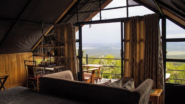 A cozy room with a large window, a wooden bookshelf, a sofa, and a dining table.